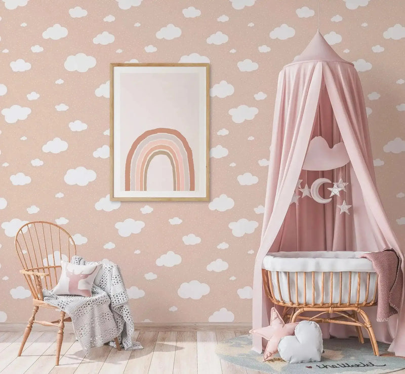 Earth's Rainbow PT Art Print displayed in a natural wood frame with white border, hung on a dusty rose wall featuring a white cloud pattern. The artwork shows a soft, hand-drawn rainbow in terracotta, peach, cream, and sage green tones on a white background. The print is styled in a nursery setting with a wicker chair, pink canopy crib with moon and star mobile, and cream knit blanket, creating a soft, calming aesthetic.