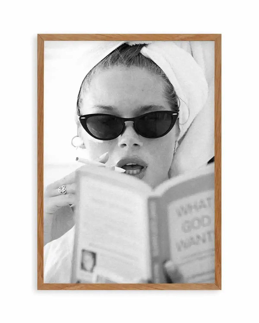 Black and white photograph titled "Easy Reading" by Mario Stefanelli, displayed in a natural wood frame with white border. The image shows a woman wearing dark sunglasses and a white head wrap, holding a magazine or publication up to her face. She wears a decorative ring and hoop earring. The photograph has a vintage aesthetic with high contrast grayscale tones and a candid, lifestyle quality.