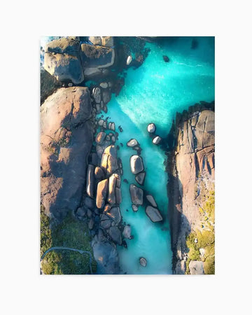 Aerial photography art print of Elephant Rocks in Western Australia, featuring a turquoise ocean inlet with large, smooth grey and brown boulders scattered throughout the water and along the rocky shorelines. The composition captures the vibrant blue of the water contrasting with the earthy tones of the rocks and surrounding green vegetation.