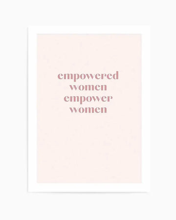 Art print featuring the phrase "empowered women empower women" in a soft, dusty rose pink, sans-serif font, centered on a pale cream background, displayed with a white border.