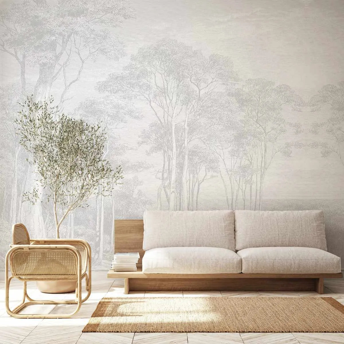 Peel and stick wallpaper mural depicting a serene forest landscape with tall eucalyptus trees rendered in soft, muted tones of cream, sage green, and pale gray. The illustration features a misty, atmospheric quality with delicate line work creating an ethereal woodland scene. The wallpaper is installed in a minimalist living room with light wood furniture, cream upholstered sofa, woven tan area rug, rattan chair, and potted eucalyptus plant, creating a cohesive natural aesthetic throughout the space.