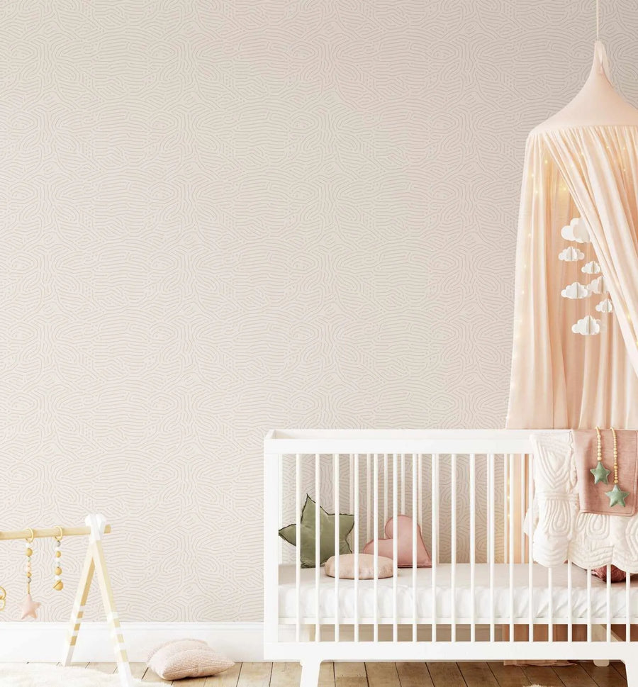 Nursery:
"Nursery room with a white crib and a light pink canopy featuring a cloud mobile, against a wall covered in Eyre Wallpaper. The wallpaper has a repeating pattern of subtle, organic, wavy lines in a light beige tone on a soft cream background, creating a textured, minimalist look. The crib contains a green star pillow, a pink heart pillow, and a small pink round pillow. A wooden play gym with hanging toys is visible on the left, and a pink knitted pillow rests on the wooden floor."