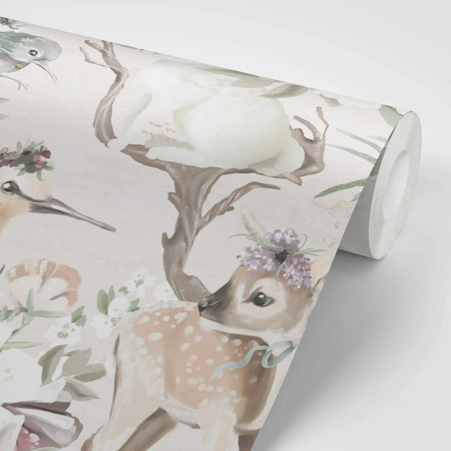 Peel and stick wallpaper featuring a repeating pattern of hand-painted forest animals and flora in soft pastel watercolours on a cream background, shown partially unrolled. The design includes a fawn with a lavender floral crown and blue ribbon, a bird with a floral crown, and a bird with a long beak, surrounded by white and peach flowers and green leaves.