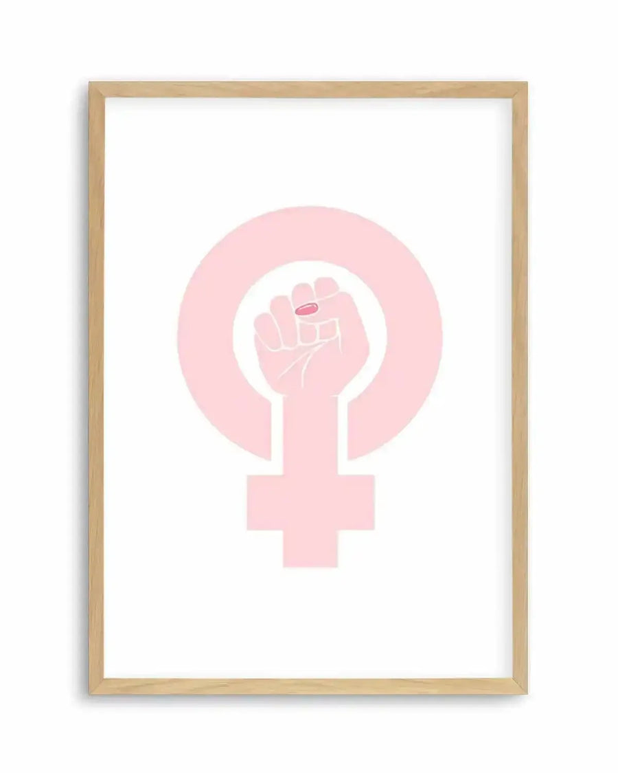 Art print featuring a pale pink female power symbol, with a raised fist in the center of the circular top portion. The fist has a small, bright pink oval on the ring finger, suggesting a ring or painted nail. The symbol is set against a clean white background and displayed in a natural oak frame with a white border.