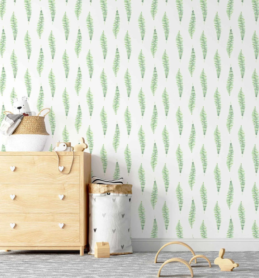 Nursery:
"Fern Foliage Wallpaper displayed in a light-filled nursery with a light wood dresser and woven basket. The wallpaper features a repeating pattern of hand-painted fern fronds in varying shades of light and medium green on a clean white background, creating a fresh, botanical feel. The dresser has white heart-shaped knobs, and the room includes a grey and white striped rug and wooden toys."