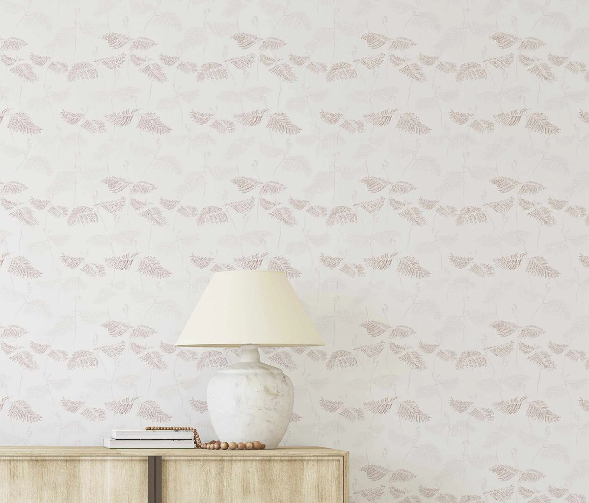 Peel and stick wallpaper featuring a repeating pattern of delicate fern fronds in burgundy and beige on a soft white background. The design has a subtle, organic quality with fine dotted texture creating the leaf patterns. A cream-colored lamp with a white ceramic base sits on a light wood cabinet in the foreground.