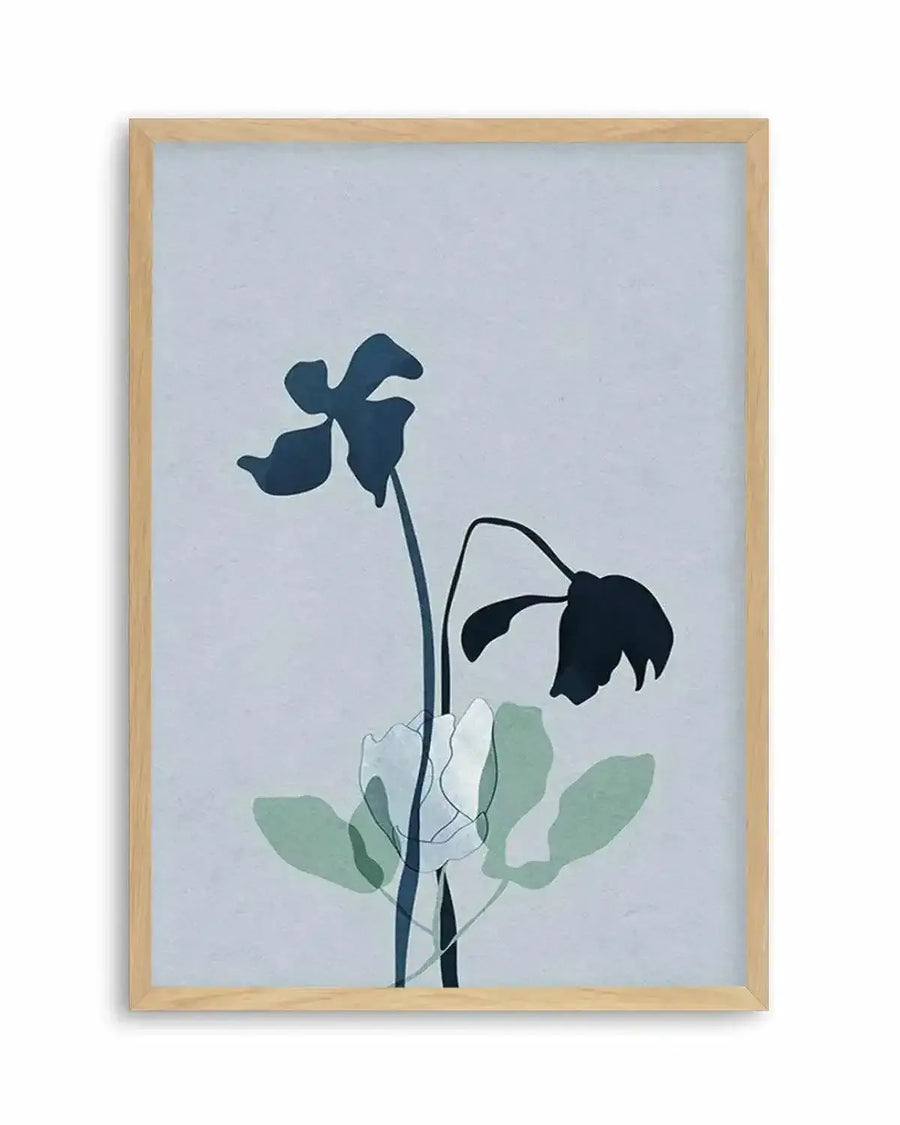 Framed art print featuring a minimalist botanical illustration with a natural wood frame. The design shows two wilting flowers with dark navy silhouetted petals against a soft blue-gray background. Delicate dark stems extend downward, accompanied by pale sage green and white watercolor-style leaves. The composition is vertical and centered, creating a contemplative mood that emphasizes the drooping, fading blooms.