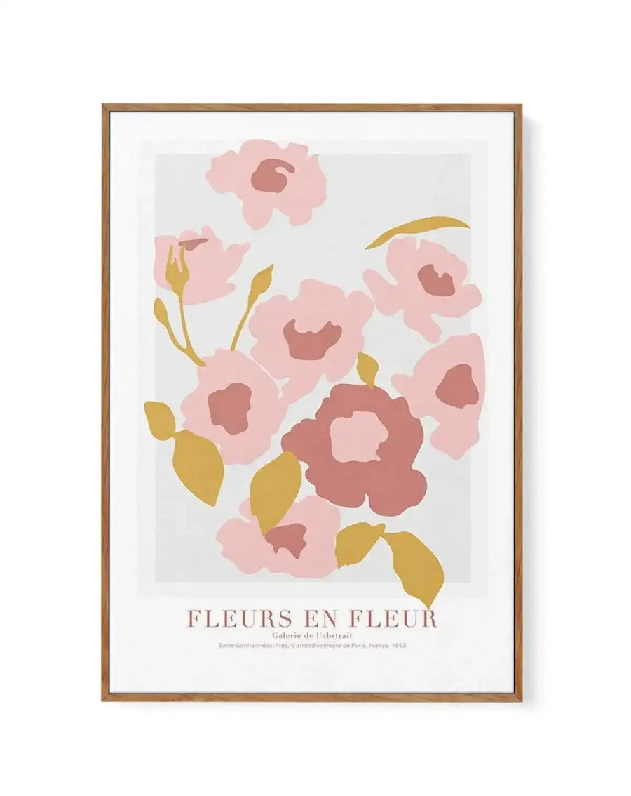 Framed canvas art print featuring an abstract botanical illustration with loose, organic flowers in soft pink and dusty rose tones, accented with golden yellow stems and leaves on a light gray background. The composition shows approximately eight stylized blooms with dark mauve centers arranged in a vertical layout. Natural wood frame with white border surrounding the artwork. Text at bottom reads "FLEURS EN FLEUR" and "Galerie de l'Abstrait" with Paris, France 1963 attribution in muted taupe lettering.