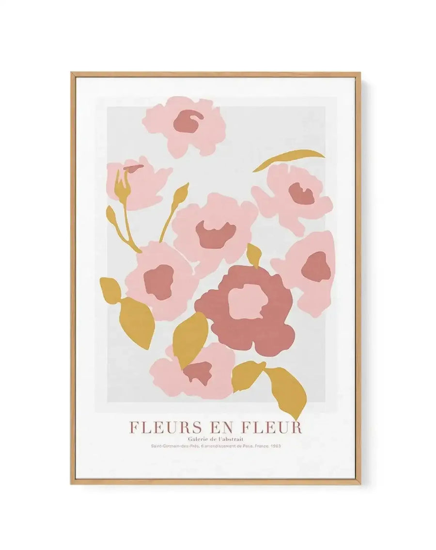 Framed canvas art print featuring an abstract floral illustration with clusters of blush pink, dusty rose, and deep terracotta flowers with rounded petals and darker centers, accented by golden yellow-green stems and leaf shapes scattered throughout a light gray background. Natural wood frame with white border. Text at bottom reads "FLEURS EN FLEUR" and "Galerie de l'Abstrait" with gallery information and 1963 date. Vertical portrait orientation.