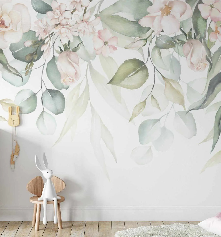 Nursery:
"Peel and stick wallpaper mural featuring a large-scale watercolour floral design with soft pink roses, white blossoms, and eucalyptus leaves in muted sage green and dusty olive on a white background, displayed in a child's room. A white bunny toy sits on a small wooden chair in the foreground, with a light grey shaggy rug on a light wood floor."