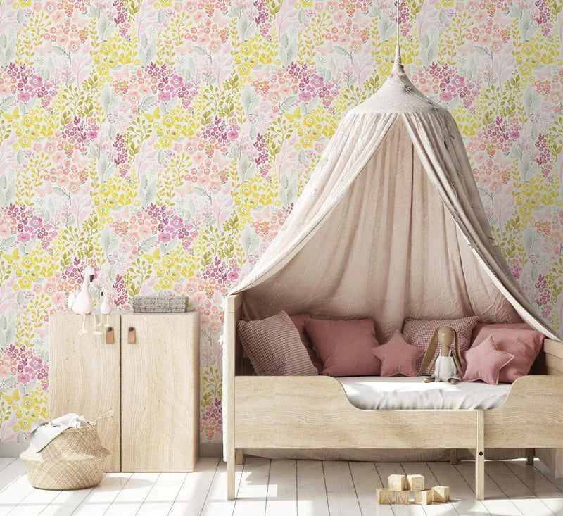 Nursery:
"Peel and stick wallpaper featuring a repeating pattern of small, hand-painted wildflowers in shades of pink, magenta, and yellow with green leaves and stems on a light cream background, displayed in a child's nursery. The wallpaper has a soft, watercolour quality. A light wood toddler bed with a cream canopy and pink pillows is on the right, and a light wood cabinet with white swan figurines and a woven basket is on the left."