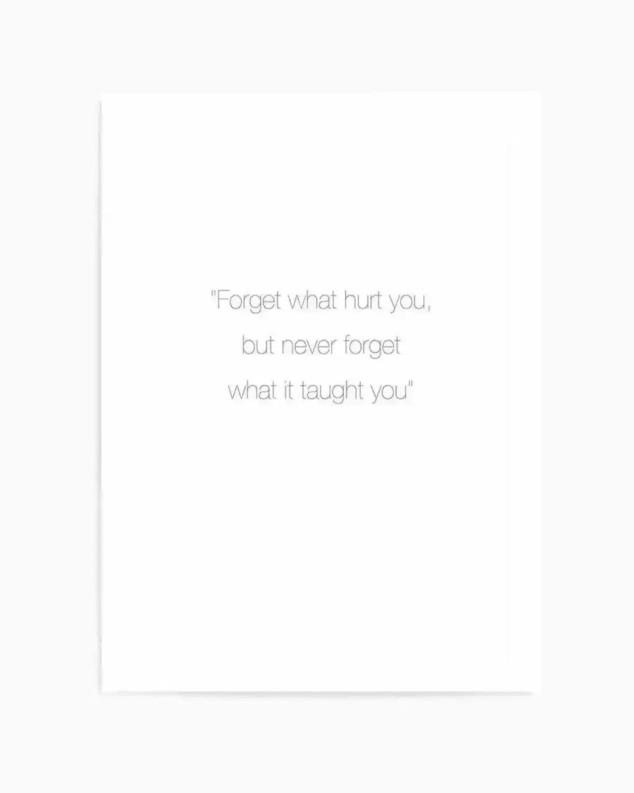 Art print featuring an inspirational quote in light gray, sans-serif typography centered on a white background. The text reads "Forget what hurt you, but never forget what it taught you" in three left-aligned lines. The print has a minimalist design with ample white space, creating a calm, reflective mood. The artwork appears to have a subtle texture with a thin vertical line visible on the left edge, suggesting a framed presentation with white border.