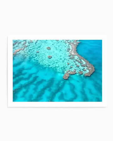 Aerial photography art print of the Great Barrier Reef with vibrant turquoise and deep blue ocean waters. The composition shows coral formations in various shades of brown and grey, creating intricate patterns and shapes against the clear water, with visible sand ripples on the seabed.