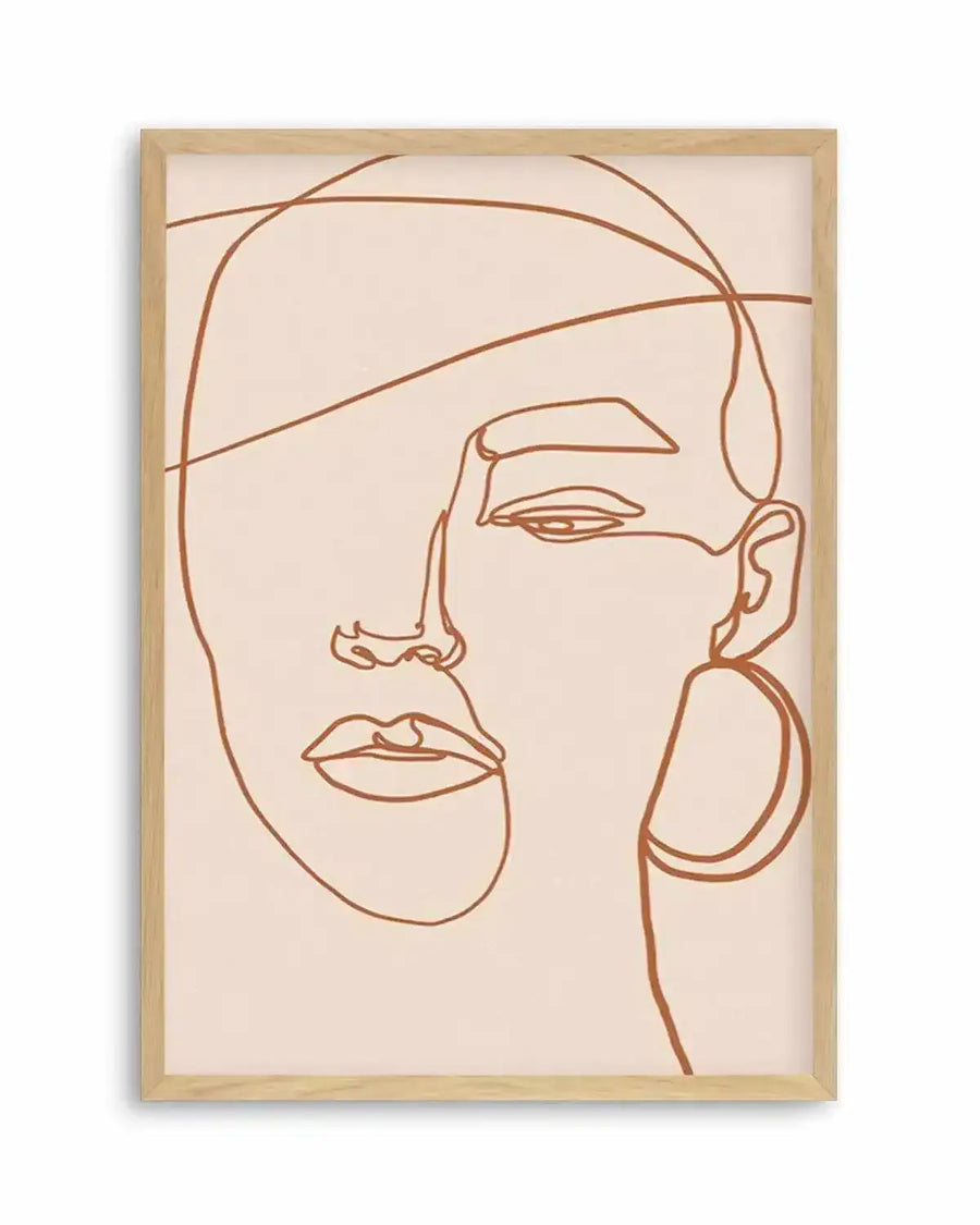 Line art print featuring a minimalist abstract female face drawn with a single continuous terracotta-coloured line on a pale cream background, displayed in a natural oak frame with white border. The face is depicted in profile, with one eye, nose, and lips visible, and a large hoop earring on the right side.