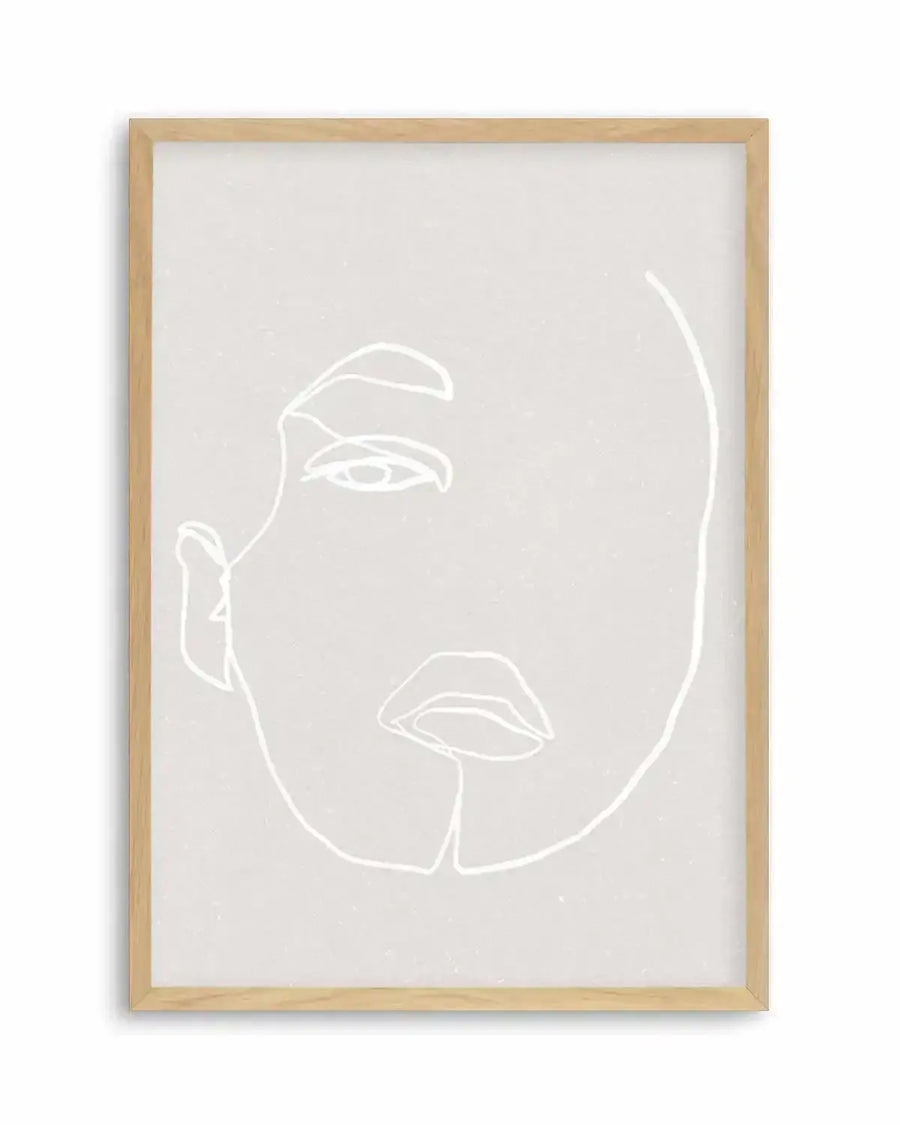 Line art print featuring a minimalist illustration of a woman's face in white on a light grey background, displayed in a natural oak frame with white border. The composition shows the left side of the face, with an eye, eyebrow, ear, and lips, rendered with continuous, flowing lines.
