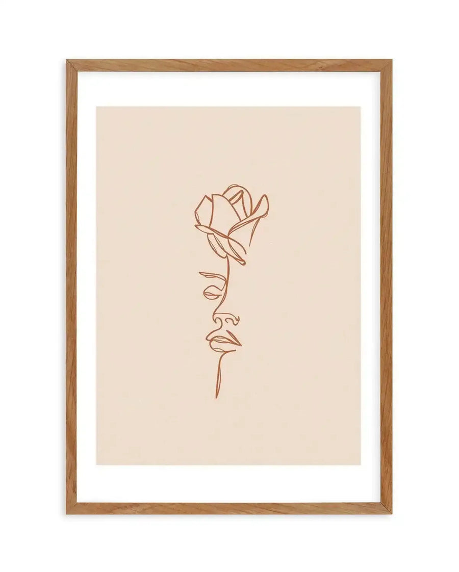 Art print featuring a minimalist one-line illustration of a rose and a woman's profile in terracotta on a cream background, printed on fine art paper and displayed in a natural oak frame with white border.