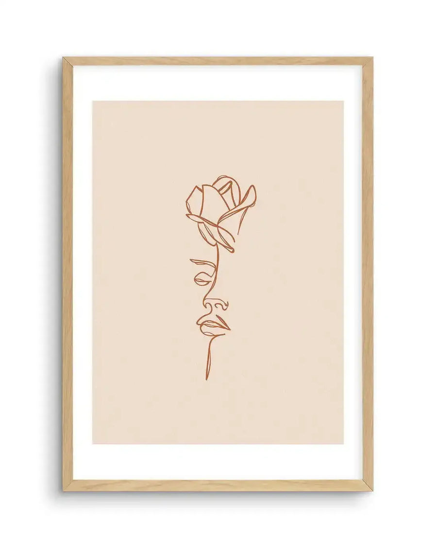 Line art print featuring a continuous single line forming the profile of a woman's face from the nose down, with a rose blooming from where her eye would be, in a warm terracotta hue on a light cream background, displayed in a natural oak frame with white border.