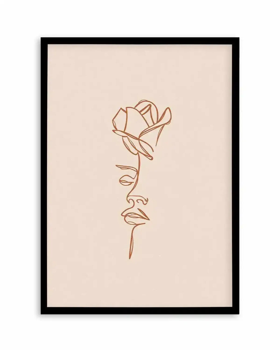Line art print featuring a minimalist illustration of a woman's face in profile, with a rose blooming from her head, drawn in a continuous terracotta-coloured line on a pale beige background, displayed in a black frame with a white border.