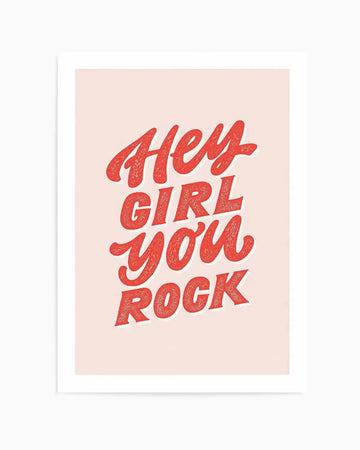 Art print featuring the hand-lettered phrase "Hey Girl You Rock" in a distressed, textured red script on a soft blush pink background. The lettering has a retro, playful style with a subtle shadow effect.