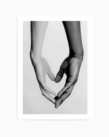 Black and white photographic art print featuring two hands, one light-skinned and one dark-skinned, forming a heart shape against a plain white background. The hands are positioned vertically, with fingers touching at the bottom to create the point of the heart and the thumbs and index fingers curving upwards to form the top arches. The image has a soft focus, highlighting the subtle textures of the skin.