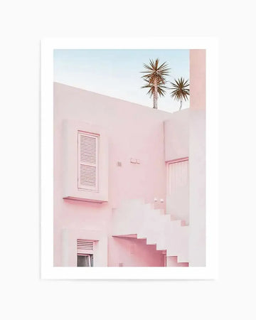 "Photography art print featuring a minimalist architectural scene in soft pastel pinks and blues. The composition shows a building with clean lines, a shuttered window, and a geometric staircase, with two palm trees visible against a clear blue sky in the upper portion of the image."
