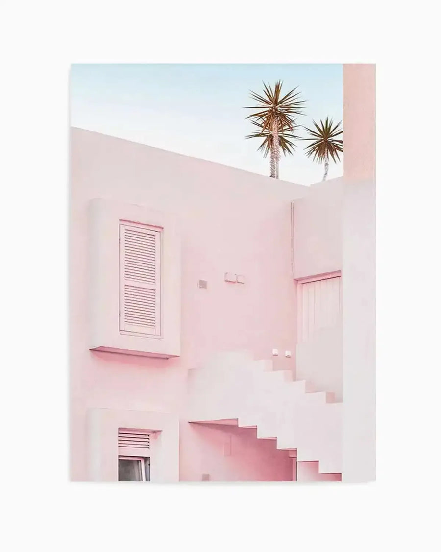 "Photography art print featuring a minimalist architectural scene in soft pastel pink and white, with two palm trees visible against a pale blue sky. The composition shows a building with a window with closed shutters, an outdoor staircase, and subtle shadows, creating a serene, modern aesthetic."