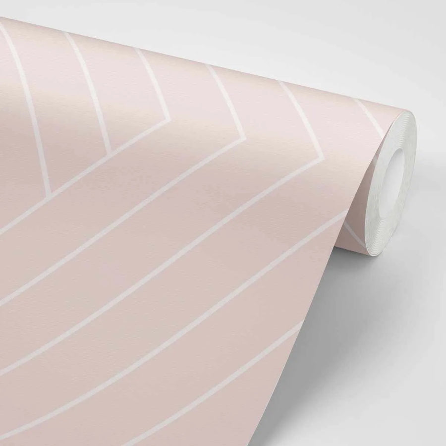 "Peel and stick wallpaper featuring a repeating geometric pattern of thick white lines forming a chevron or herringbone design on a soft blush pink background. The lines create a sense of movement across the textured surface of the wallpaper."