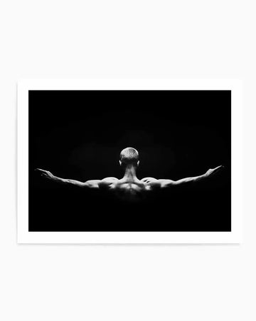Framed black and white photograph of a man from behind, with his arms outstretched to the sides, against a dark background. The man has short hair and visible muscle definition in his back and arms, with subtle lighting highlighting his form. The print is displayed in a white frame with a white border.