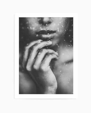 Black and white art print featuring a close-up, out-of-focus photograph of a person's face and hand behind a rain-streaked window. The person's lips are slightly parted, and their hand is raised to their chin, with fingers gently touching their lower lip. The rain droplets on the glass create a blurred, textured effect over the face and hand, adding to the moody and contemplative atmosphere.
