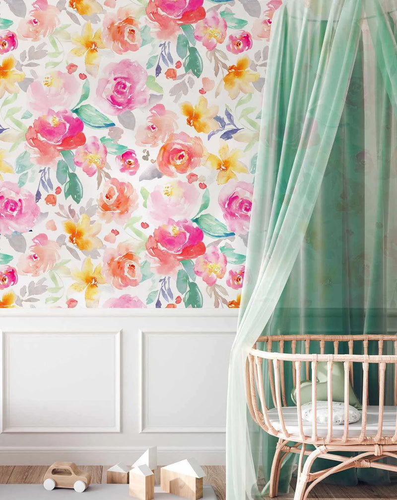 Nursery:
"Wallpaper featuring a repeating pattern of large-scale watercolour flowers in shades of hot pink, blush pink, coral, and sunny yellow with sage green and grey leaves, displayed on a wall above white wainscoting in a nursery. A light wood rattan bassinet with a mint green canopy is visible on the right, and wooden toys are on the floor."