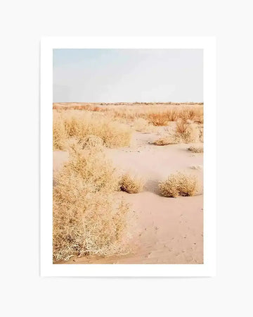 Product shot art print (photography):
Framed photograph of a desert landscape with a pale blue sky and light tan sand. The foreground features numerous dried, light brown tumbleweeds and sparse, darker brown bushes. The composition shows a vast, flat expanse of desert under a bright, clear sky.