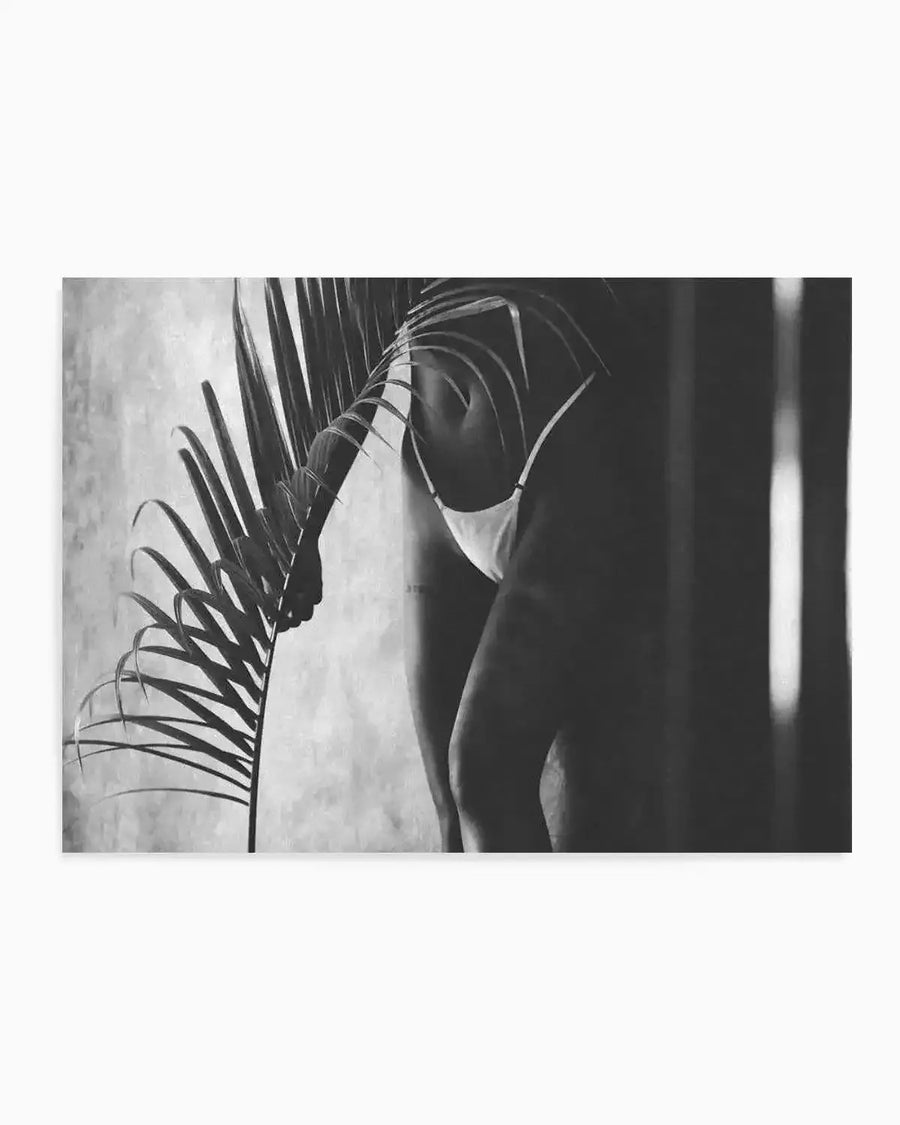 Black and white art print titled Island Bliss by Mario Stefanelli featuring a woman in a sleeveless top viewed from behind, holding palm fronds against her body. The photograph-style composition shows dramatic contrast between light and shadow, with the woman's silhouette prominent against a textured, light background. Palm leaves create linear patterns across the composition. The artwork conveys a contemplative, tropical mood through its monochromatic tones and intimate framing.