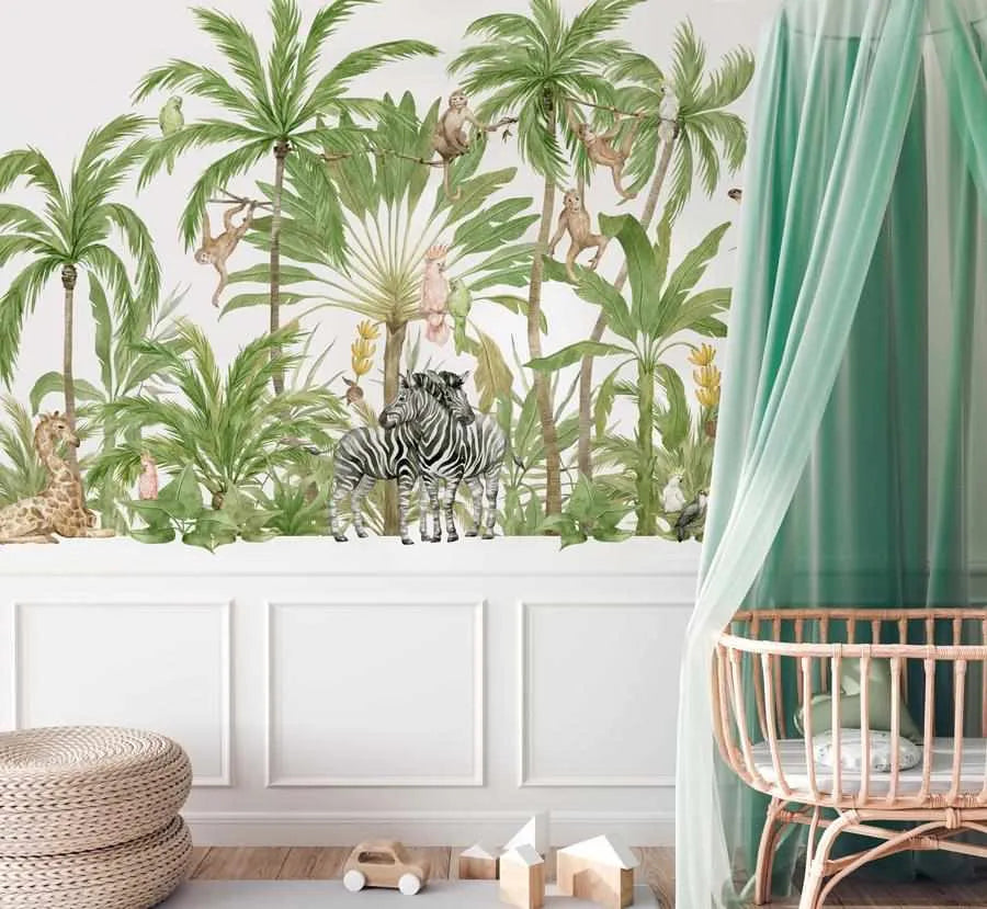 Lifestyle shot of a nursery featuring a peel and stick wallpaper mural with a jungle scene. The mural depicts a lush tropical forest with various palm trees and other green foliage, with several animals including two zebras standing side-by-side in the foreground, a giraffe lying down on the left, and monkeys and birds perched among the trees. The room has white wainscoting and a light wood floor, with a woven ottoman on the left and a light wood crib with a sheer green canopy on the right.