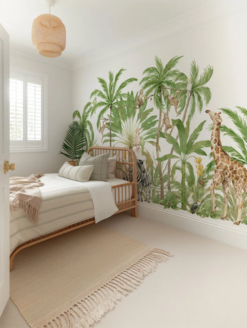 A child's bedroom with a jungle-themed peel and stick wallpaper mural covering the lower half of the wall. The mural features hand-painted palm trees and large tropical leaves in various shades of green, with a giraffe, zebras, monkeys, and tropical birds. The room includes a light wood rattan bed with striped bedding, a textured cream rug, and a woven pendant light.