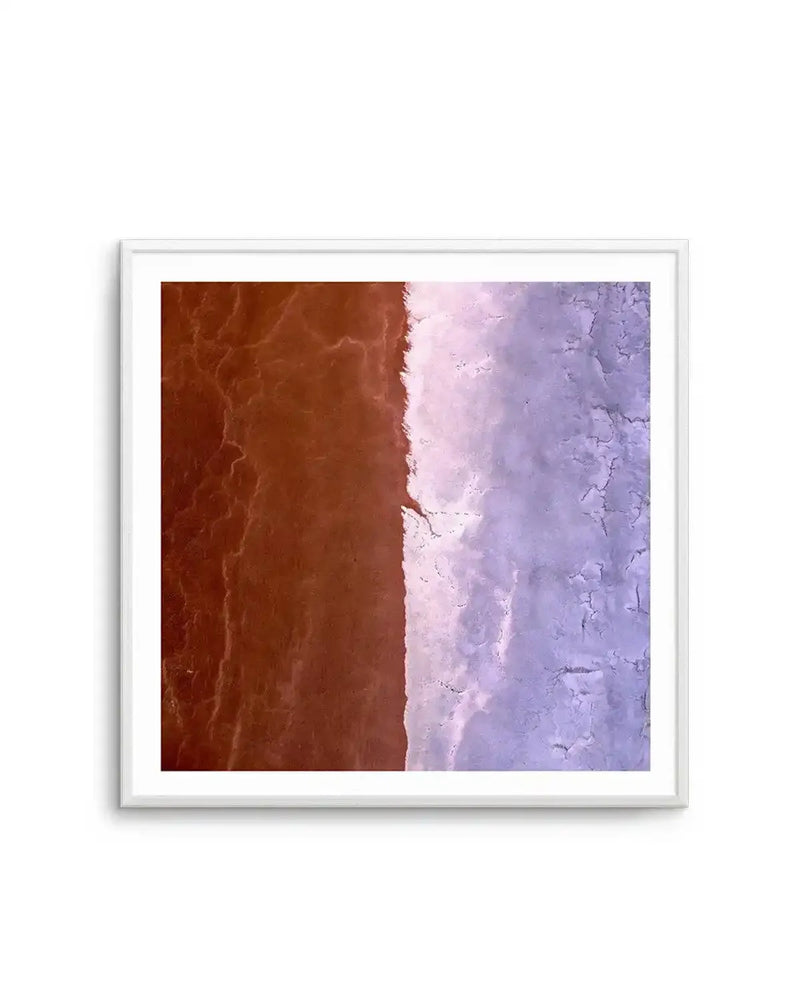 Framed aerial photography art print of Kati Thanda-Lake Eyre, featuring a stark vertical division between deep reddish-brown earth on the left and a textured, pale lavender and white salt crust on the right, displayed in a white frame with white border.