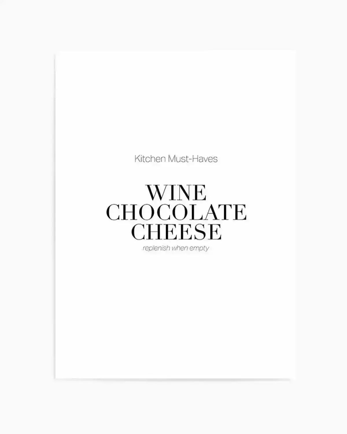 A minimalist art print featuring the text "Kitchen Must-Haves" in small gray letters at the top, followed by "WINE CHOCOLATE CHEESE" in large black serif capital letters in the center, with "replenish when empty" in small gray italicized text below. The design is set against a clean white background with a light gray vertical line on the left edge, creating a modern, typographic aesthetic with ample white space throughout.