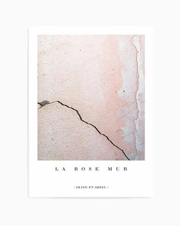 Art print titled "La Rose Mur" featuring a close-up photograph of a weathered wall with peeling plaster in soft blush pink and cream tones. A dark diagonal crack runs across the textured surface. The print is mounted on a white background with the title in elegant sans-serif typography below the image and artist credit "Olive et Oriel" at the bottom.