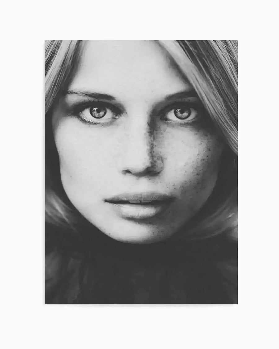 Black and white photographic art print featuring a close-up portrait of a young woman with long blonde hair and freckles, looking directly at the viewer with an intense gaze. The composition captures fine skin texture and the subtle reflections in her eyes.