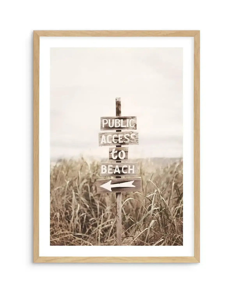 Framed sepia-toned photograph of a weathered wooden signpost in tall, dry grass, pointing towards a beach, with a natural wood frame and white border. The sign reads "PUBLIC ACCESS to BEACH" with a white arrow pointing left.