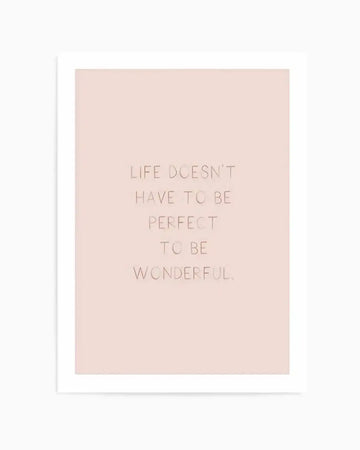 Art print with blush pink background featuring centered text in soft taupe that reads "LIFE DOESN'T HAVE TO BE PERFECT TO BE WONDERFUL" in a modern sans-serif font. The print is mounted on a white backing board, creating a clean white border around the design. Minimalist composition with ample negative space emphasizing the inspirational message.