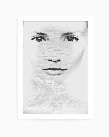 Black and white double exposure art print featuring a woman's face with serene, direct gaze overlaid with ocean waves and water textures across the center and lower portion. The illustration uses fine line work for facial features—defined eyes with long lashes, delicate nose, and neutral lips—while water photography creates an ethereal, flowing effect through the middle of the composition. Mounted in a white frame with white border on a light background.
