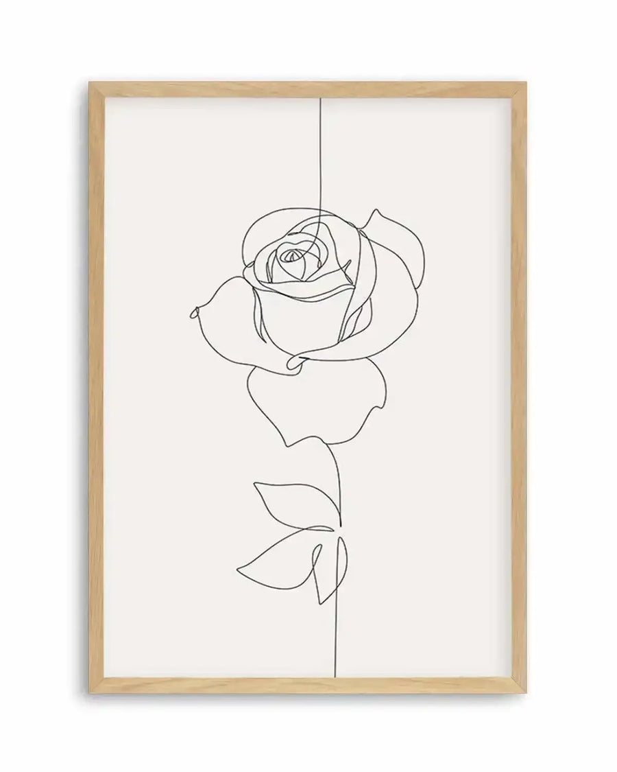 Line art print featuring a single rose in black outline on a white background, printed on fine art paper and displayed in a natural oak frame with white border. The rose is depicted with a continuous, flowing line, showing the petals of the bloom and two leaves on the stem.