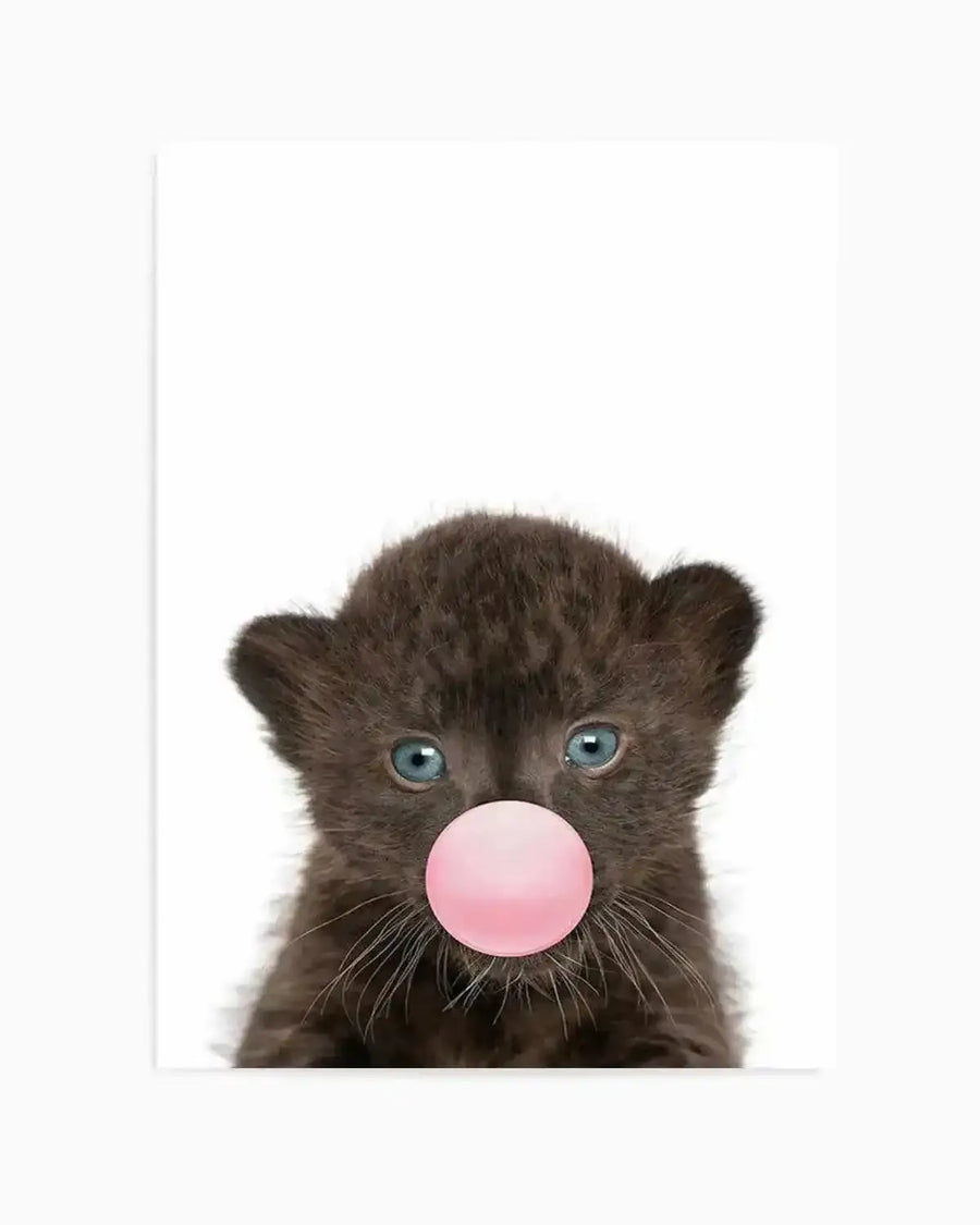 Art print featuring a close-up portrait of a young black leopard cub with striking blue-grey eyes and delicate white whiskers against a white background. The cub blows a large, glossy bubble gum bubble in soft pink. The photograph-style image is printed on white paper with a thin grey vertical line visible on the left edge, suggesting gallery-style framing or mounting.