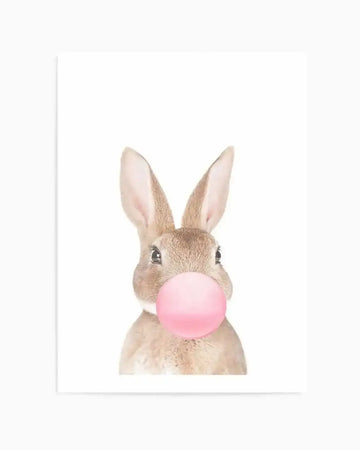 Art print featuring a young rabbit with tan and cream fur and long upright ears facing forward, blowing a large bubble gum bubble in soft pink. The illustration has a gentle, whimsical style rendered in soft watercolor tones. White background with white border and frame.