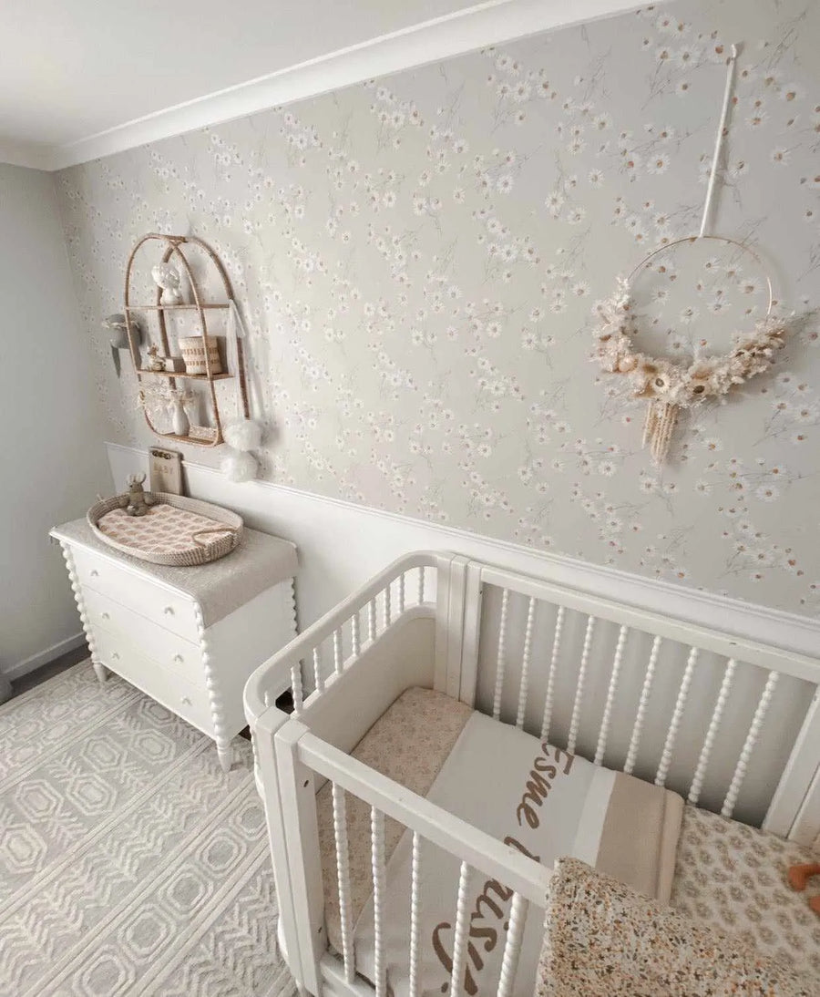 Nursery:
"A baby nursery featuring a white crib and changing table against a wall with Little Daisy Chain wallpaper. The wallpaper has a repeating pattern of small, delicate white daisy-like flowers with faint yellow-brown centers and thin green stems on a soft, light grey background. The room includes a light-colored patterned rug, a decorative gold hoop with dried flowers, and a gold-toned wall shelf with various white and cream decorative items."