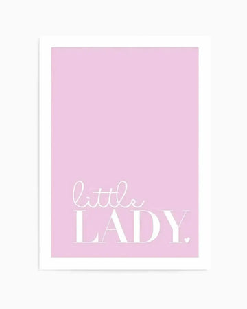 Art print featuring the text "little LADY" in white lettering on a soft pink background. The word "little" is written in a delicate cursive script, while "LADY" appears in larger, bold sans-serif capitals. A small white heart symbol is positioned to the right of the text. The print is mounted in a white frame with a white border and displayed against a neutral background.
