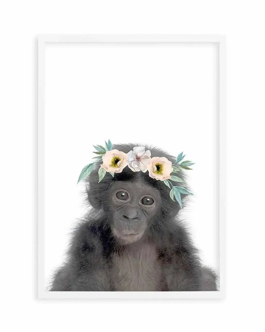 Watercolour art print featuring a baby chimpanzee wearing a flower crown, displayed in a white frame with white border. The chimpanzee has dark fur and large, dark eyes, looking directly forward with a gentle expression. The flower crown consists of light pink, cream, and white flowers with green leaves.