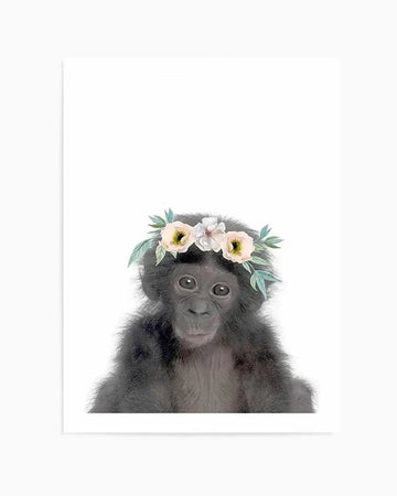 Art print featuring a baby chimpanzee with dark grey fur and large, dark eyes, wearing a delicate flower crown with pale yellow, white, and blush pink blossoms and soft green leaves, set against a clean white background.