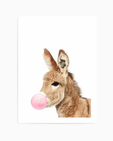 "Photography art print featuring a baby donkey in profile, facing right, against a stark white background. The donkey has soft, light brown fur and is blowing a bright pink bubblegum bubble from its mouth. The composition captures the donkey's gentle expression and the playful bubble."