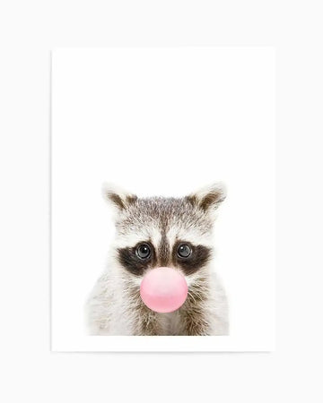 "Photography art print featuring a baby raccoon with a pink bubblegum bubble emerging from its mouth, set against a stark white background. The raccoon has dark grey and white fur, with distinctive black markings around its large, dark eyes, creating a playful and curious expression. The pink bubble is perfectly round and glossy, contrasting with the raccoon's soft, textured fur."